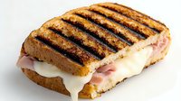 Grilled sandwich with melted mozzarella cheese and ham on toasted bread, showing grill marks and oozing cheese, photographed on white background for menu or food service.
