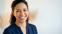 Happy Hispanic female healthcare professional with braces smiling warmly in medical office wearing navy scrubs for dental or medical practice marketing.