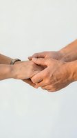 Elderly couple holding hands tenderly, showing love, support, and togetherness in a close-up shot against a light background.