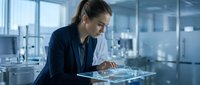 Woman engineer examining circuit board in modern laboratory environment with advanced technology equipment and glass partitions.