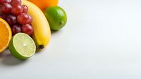 Fresh colorful fruits including grapes, banana, orange and lime arranged on white background with copy space for healthy eating concepts.