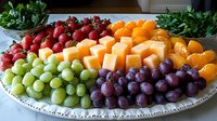 Fresh fruit platter with colorful assortment of grapes, cantaloupe, strawberries, mandarin oranges and garnish on decorative serving plate, arranged for party or event.