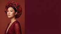 Young Asian woman wearing elegant burgundy headwrap and matching textured garment against warm red background. Fashion and beauty portrait for editorial and lifestyle design use.