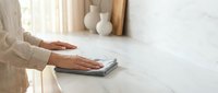 Woman hands cleaning white marble kitchen counter with gray microfiber cloth in bright modern home interior for hygiene and housework maintenance.