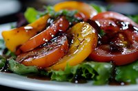 Fresh heirloom tomato salad with mixed greens, balsamic glaze and herbs on white plate. Colorful summer vegetarian dish for healthy eating and restaurant menu.