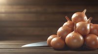 Fresh brown onions on rustic wooden table with knife blade in soft natural lighting, moody food photography composition for restaurant menu and cooking blogs.