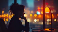 Silhouette of woman looking through window at night with urban bokeh lights creating atmospheric mood for contemplative moments.