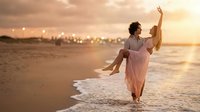 Young couple dancing on beach at sunset with romantic golden light and ocean waves creating dreamy atmosphere for wedding or honeymoon celebration.