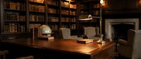 Elegant vintage library interior with wooden desk, brass lamp, and floor-to-ceiling bookshelves creating warm scholarly atmosphere for reading and study.