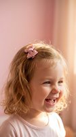 Happy blonde toddler girl with pink hair bow smiling joyfully in soft natural light. Cheerful child portrait for family lifestyle content.