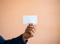 Male hand holding blank white card against neutral beige background. Isolated on solid color for mockup, branding, advertising, and promotional design use.
