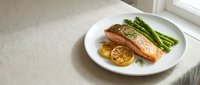Grilled salmon fillet with roasted lemon slices and fresh green beans on white plate, gourmet dinner presentation for culinary and food styling projects.