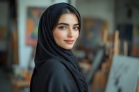 Young woman wearing traditional black hijab smiling confidently at camera with natural makeup and gentle expression against blurred artistic background.