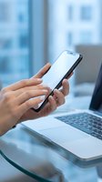 Professional using smartphone at modern office desk with laptop computer for business communication and digital workflow management.