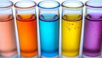 Colorful liquid samples in glass test tubes arranged in row showing gradient from pink through orange, blue, yellow to purple, laboratory research concept.