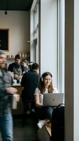Young woman of mixed ethnicity working on laptop in casual coffee shop setting with diverse customers and staff in background, ideal for business, technology, and lifestyle content.