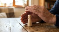 Senior hands protecting wooden figure on rustic table symbolizing care, insurance coverage, family protection, and security in warm home setting.
