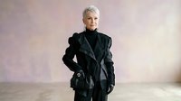 Senior woman with short white hair wearing black leather jacket and dark clothing, standing confidently against neutral studio background. Suitable for business, fashion, lifestyle and corporate projects.