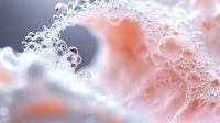 Macro photography of soap foam bubbles in coral pink and white colors creating abstract organic texture with soft bokeh effect for cosmetic backgrounds.