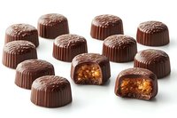 Round milk chocolate pralines with caramel and nuts filling arranged on white background, two candies cut in half showing rich interior texture and layers.