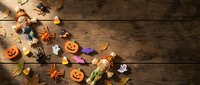 Halloween decorations scattered on rustic wooden background with pumpkins, spiders, candy corn, ghosts and autumn leaves for seasonal crafting projects.