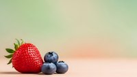 Fresh strawberry and blueberries on wooden surface with soft gradient background for healthy eating and nutrition concepts.