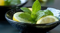 Fresh mint leaves and lemon slices in dark textured bowl with water droplets for refreshing summer drinks and culinary garnish applications.