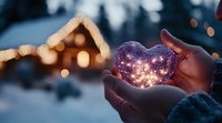 Glowing heart-shaped crystal ball held in winter gloves against snowy evening background with illuminated cabin and magical bokeh lights creating romantic atmosphere.