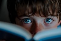 Young boy with striking blue eyes and freckles reading book in soft natural light. Educational learning concept for children literature and storytelling.