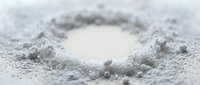 Circular hole surrounded by white powder or flour on flat surface, shallow depth of field effect, close-up macro shot.
