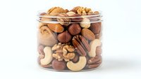 Mixed nuts and dried fruits in glass jar isolated on white background for healthy snacking and cooking recipes.