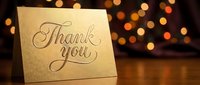 Elegant gold thank you card with cursive lettering on wooden surface, warm bokeh lights background, suitable for greeting cards, invitations, and thank you notes.