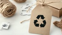Recycling symbol on kraft paper tag with twine and eco-friendly packaging materials on white background. Sustainable lifestyle and zero waste concept.