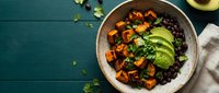 Overhead view of a nutritious grain bowl with roasted sweet potato, black beans, fresh cucumber slices, and herbs on teal wooden surface. Healthy meal prep.
