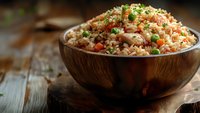 Steaming fried rice with vegetables and chopped green onions served in wooden bowl on rustic table, close up view with selective focus and copy space.