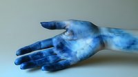 Blue painted hand with cosmic galaxy pattern reaching out against neutral background for artistic and creative design projects.
