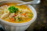 Homemade chicken noodle soup with tender meat, pasta, carrots and fresh parsley garnish in white ceramic bowl on dark counter, comfort food styling.