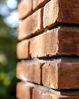 Close-up view of red brick wall corner showing textured masonry detail, mortar joints, and selective focus with natural outdoor lighting and bokeh background.