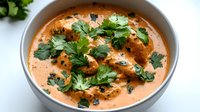 Creamy butter chicken curry garnished with fresh cilantro leaves in gray ceramic bowl. Traditional Indian cuisine with rich orange-colored sauce and tender meat pieces.