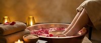 Woman soaking feet in wooden bowl with rose petals and warm water for spa relaxation, wellness and self-care treatment at home or luxury spa.