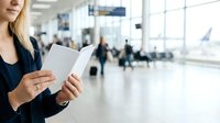 Woman holding passport in airport terminal with travelers and departure boards in background, travel documentation and international journey concept.