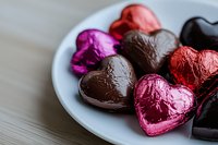 Heart shaped chocolate candies wrapped in colorful red, pink and black foil arranged on white plate. Sweet romantic treats for Valentine's Day celebration.