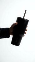 Hand holding a black insulated stainless steel tumbler with straw on white background, showcasing modern reusable drinkware for eco-friendly lifestyle.