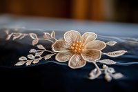 Delicate floral embroidery detail on dark fabric showcases intricate beadwork and cream-colored thread creating elegant flower and leaf pattern.