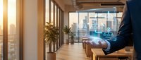 Young professional man in business suit sitting at wooden desk in modern office with floor-to-ceiling windows overlooking city skyline during golden hour, working on laptop for corporate business concepts.