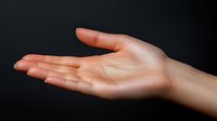 Elegant female hand with natural manicure extended in welcoming gesture against dark background, showing open palm in horizontal position.