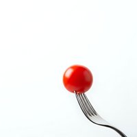 Fresh red cherry tomato on silver fork isolated on white background for culinary and healthy eating concepts.