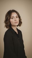 Professional young woman with short brown hair in black shirt portrait on neutral beige background for business and corporate use.