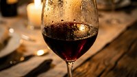 Glass of red wine with condensation droplets on elegant wooden table in warm candlelit restaurant setting for dining and hospitality concepts.