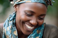Young African woman with bright smile wearing colorful turquoise headscarf, expressing joy and happiness in natural outdoor setting.